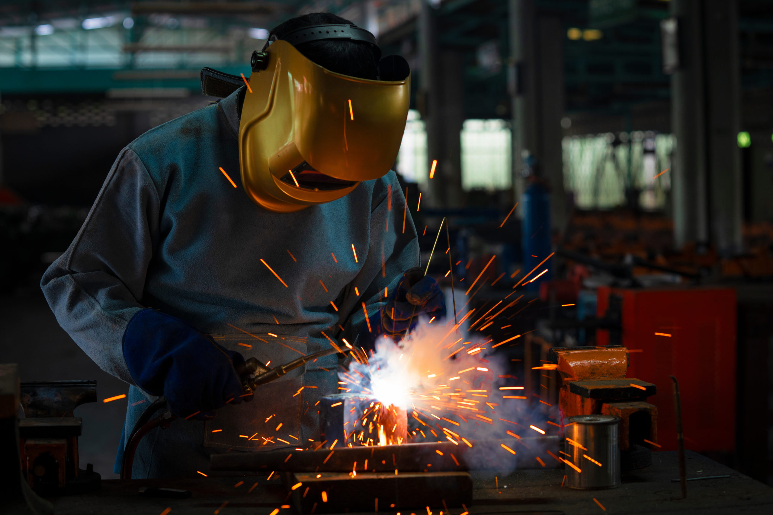 Industrial welder is welding metal part in the factory